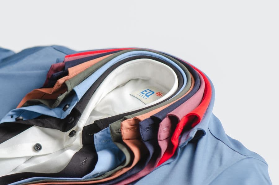 A fanned stack of work shirts in a dozen colourways, collars and button plackets showing, on a plain studio background.