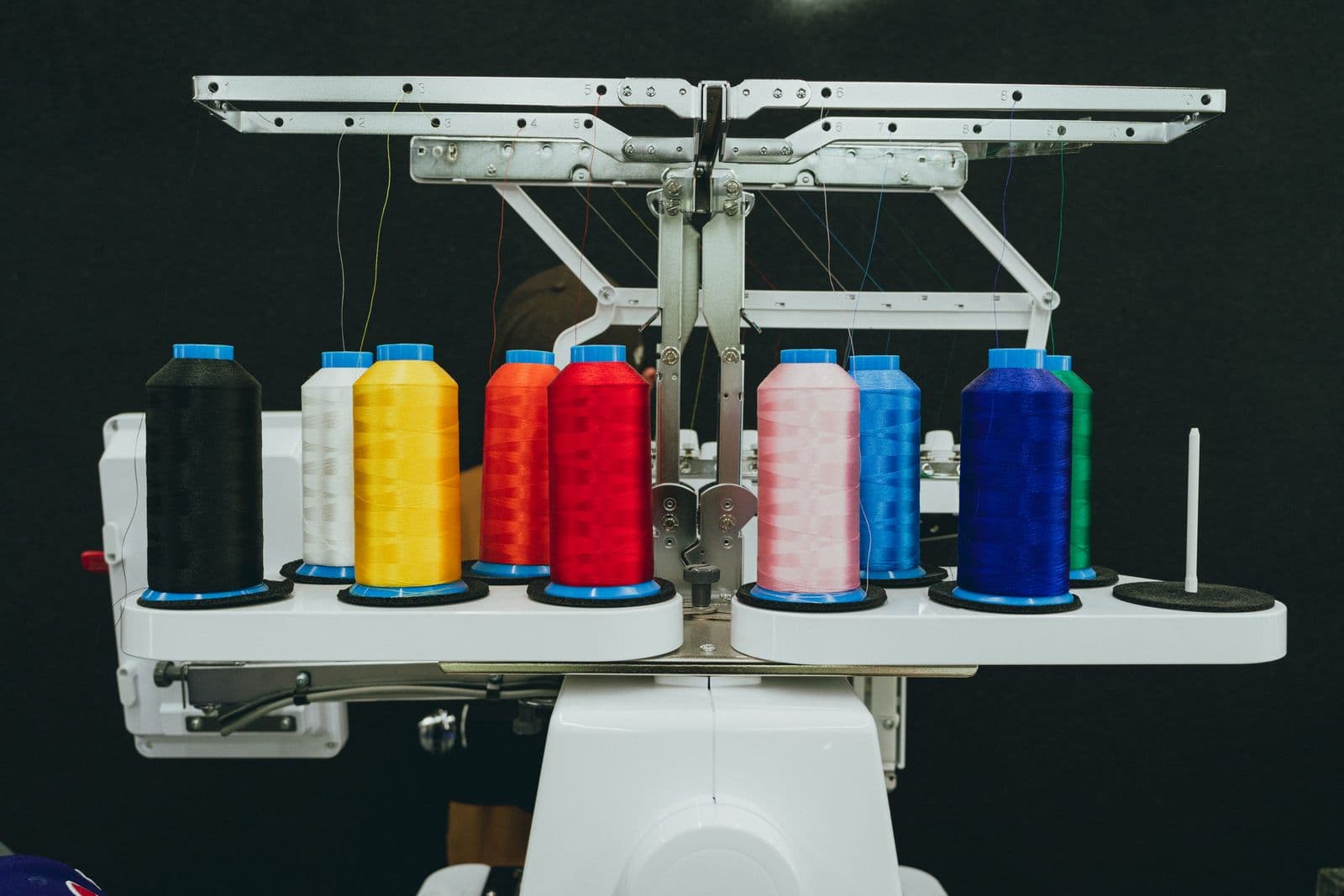 A rack of embroidery thread cones in mixed colours on a workshop wall, the working stock of a decoration floor.