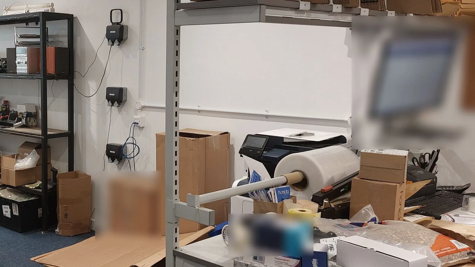 A packing station with a worktop, stacked boxes, packing materials and a shutter door behind.