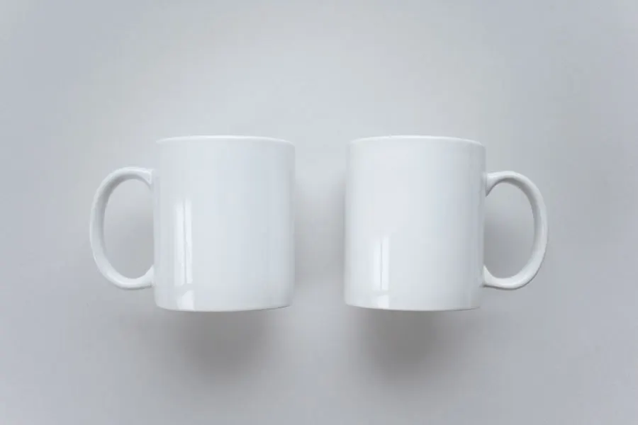 Two plain white ceramic mugs, handles outward, side by side on a white surface.