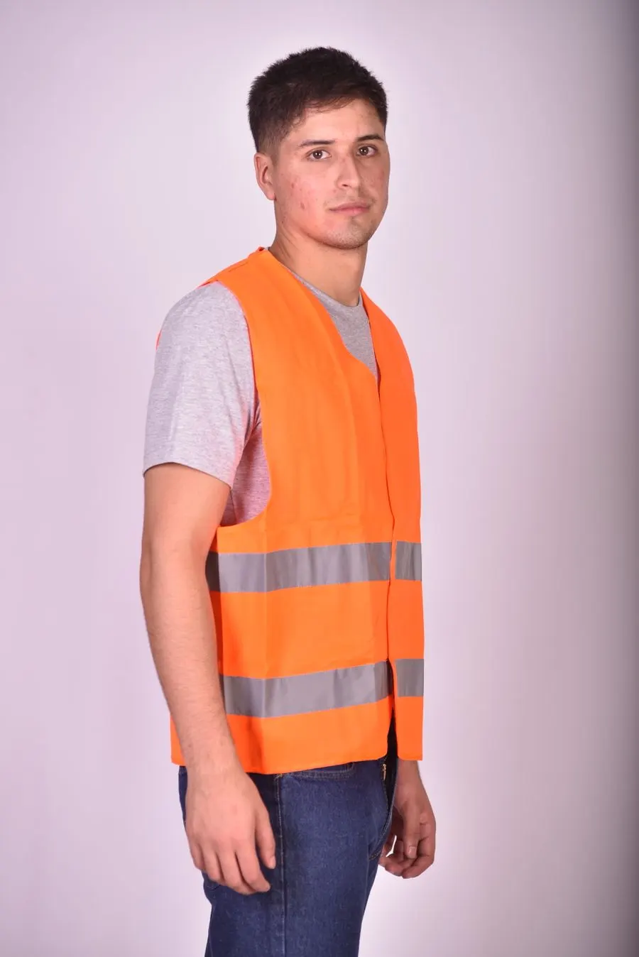 A worker in a grey T-shirt wearing an orange hi-vis vest with two reflective bands, photographed against a plain studio backdrop.